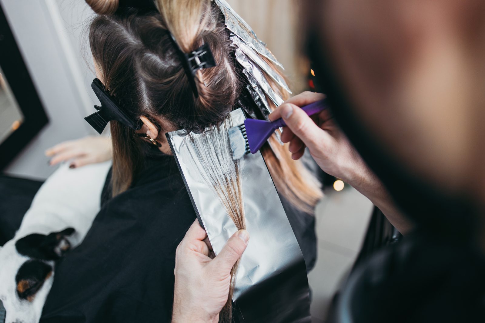 Stylist painting lightener onto a client's hair over foil during a highlighting service at a salon