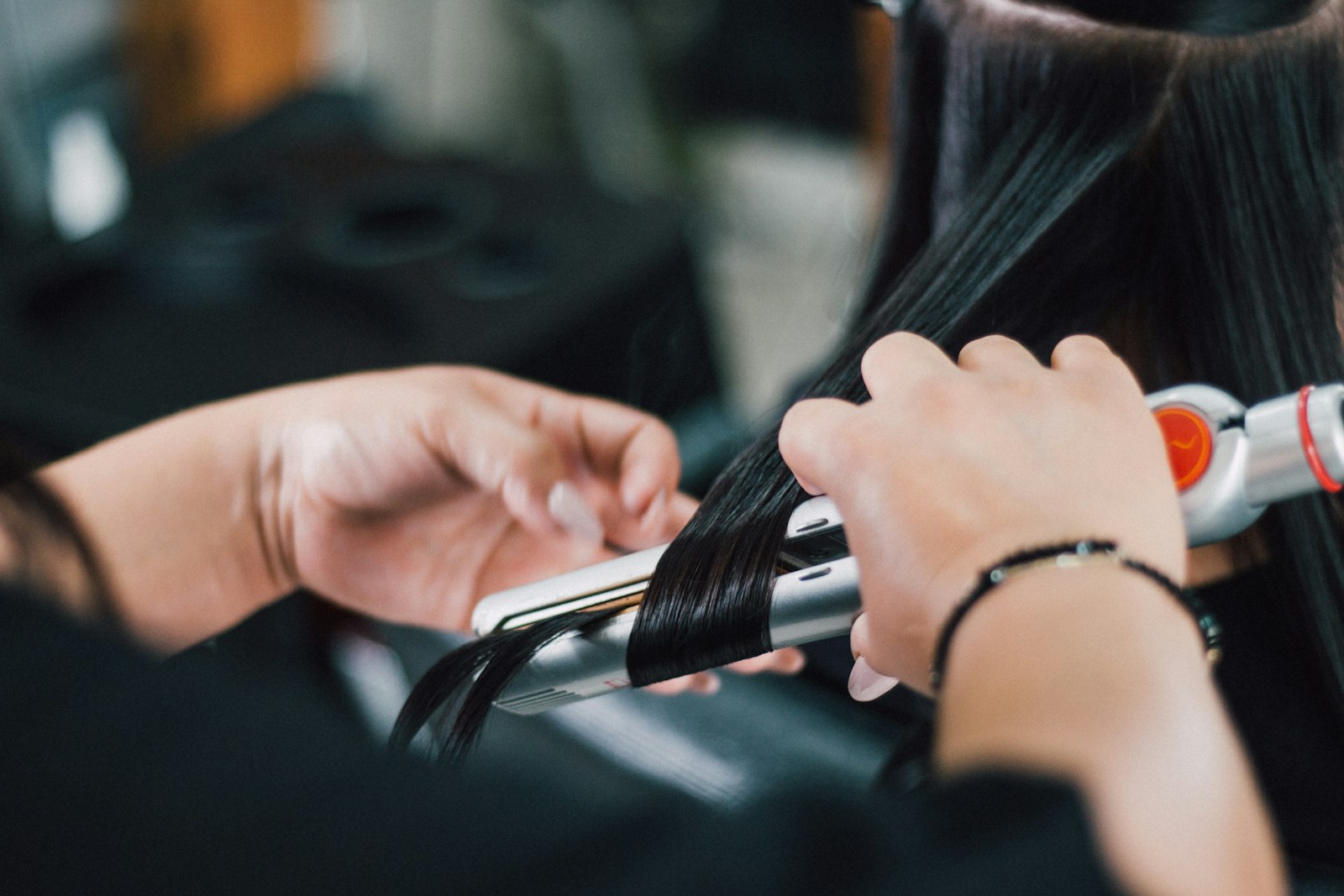Stylist gliding a flat iron through a section of smooth, glossy dark hair during a salon smoothing treatment