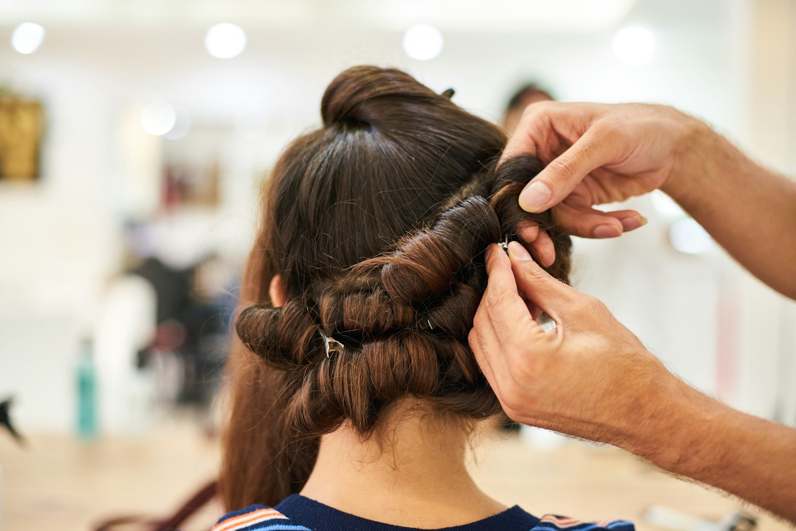 Stylist carefully winding a guest's dark hair onto rollers for a permanent wave set in a salon